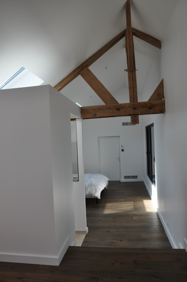 Imagen de dormitorio principal industrial grande sin chimenea con paredes blancas, suelo de madera oscura y suelo marrón