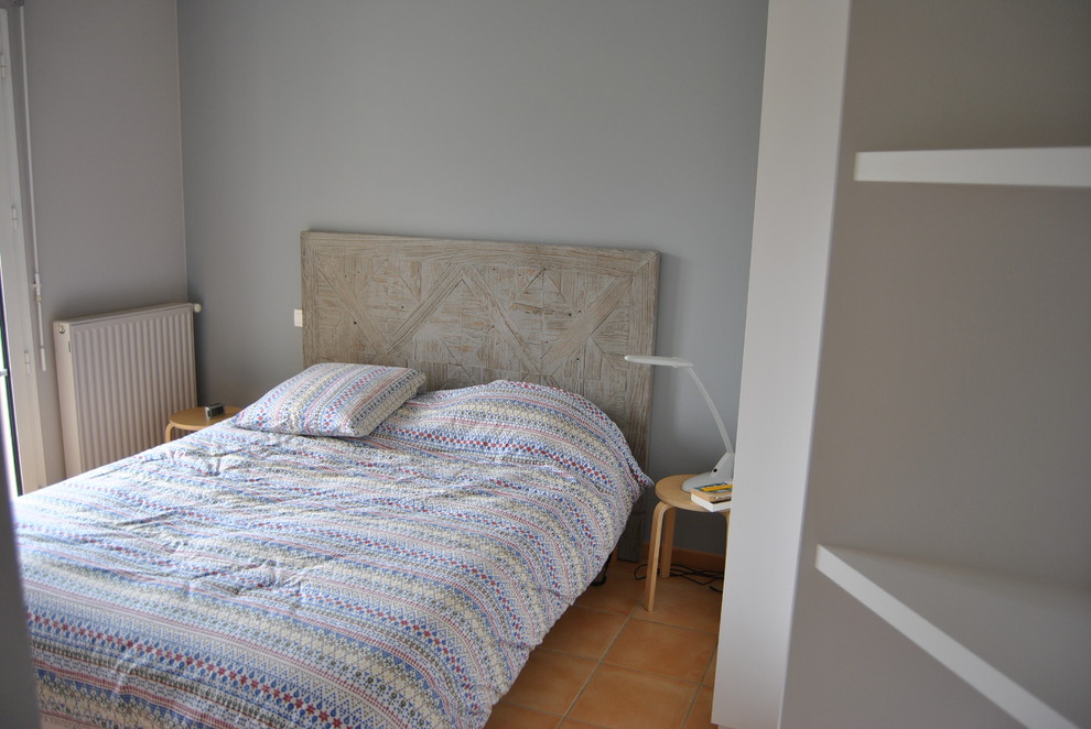 Cette image montre une petite chambre d'amis minimaliste avec un mur gris, tomettes au sol et aucune cheminée.