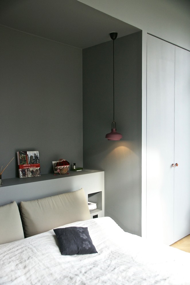 Cette image montre une chambre parentale design de taille moyenne avec un mur gris, parquet clair, une cheminée d'angle, un manteau de cheminée en plâtre et un sol beige.