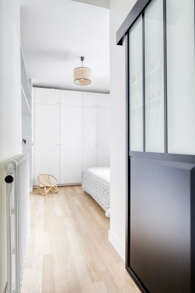 Ejemplo de habitación de invitados actual de tamaño medio sin chimenea con paredes blancas, suelo de madera clara y suelo marrón