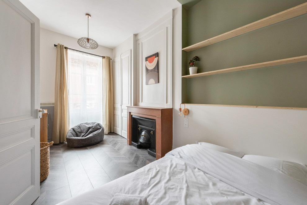Immagine di una grande camera da letto design con pareti verdi, pavimento in laminato, camino classico, cornice del camino in pietra e pavimento grigio