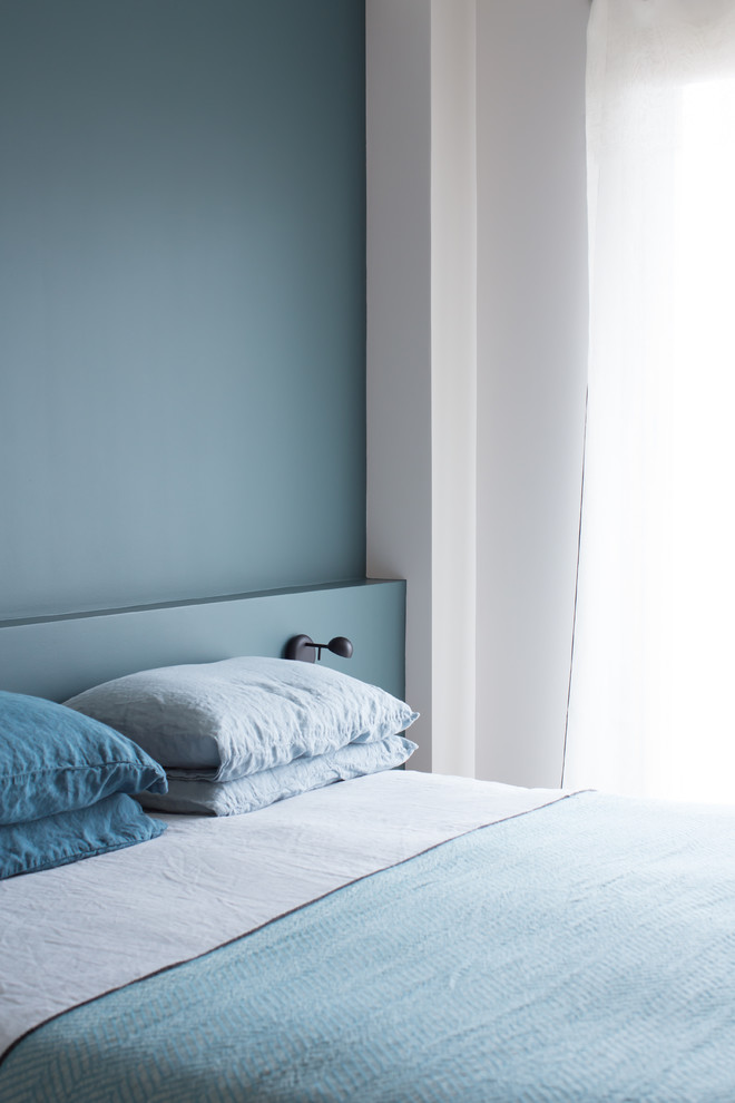 Cette image montre une petite chambre parentale nordique avec un mur bleu et un sol en bois brun.