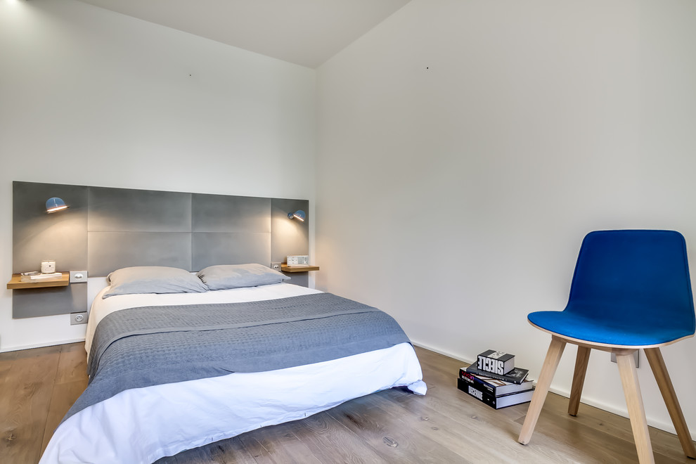 Diseño de dormitorio principal y gris y blanco escandinavo de tamaño medio sin chimenea con paredes blancas, suelo de madera en tonos medios y suelo marrón