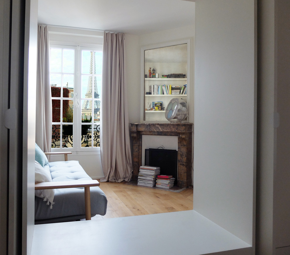 Ejemplo de habitación de invitados actual de tamaño medio con paredes blancas, suelo de madera clara, chimenea de esquina, marco de chimenea de piedra y suelo beige