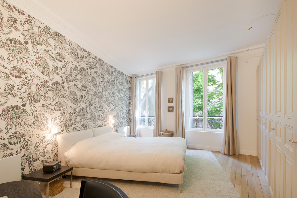 Large contemporary master bedroom in Paris with white walls, light hardwood flooring, no fireplace and brown floors.
