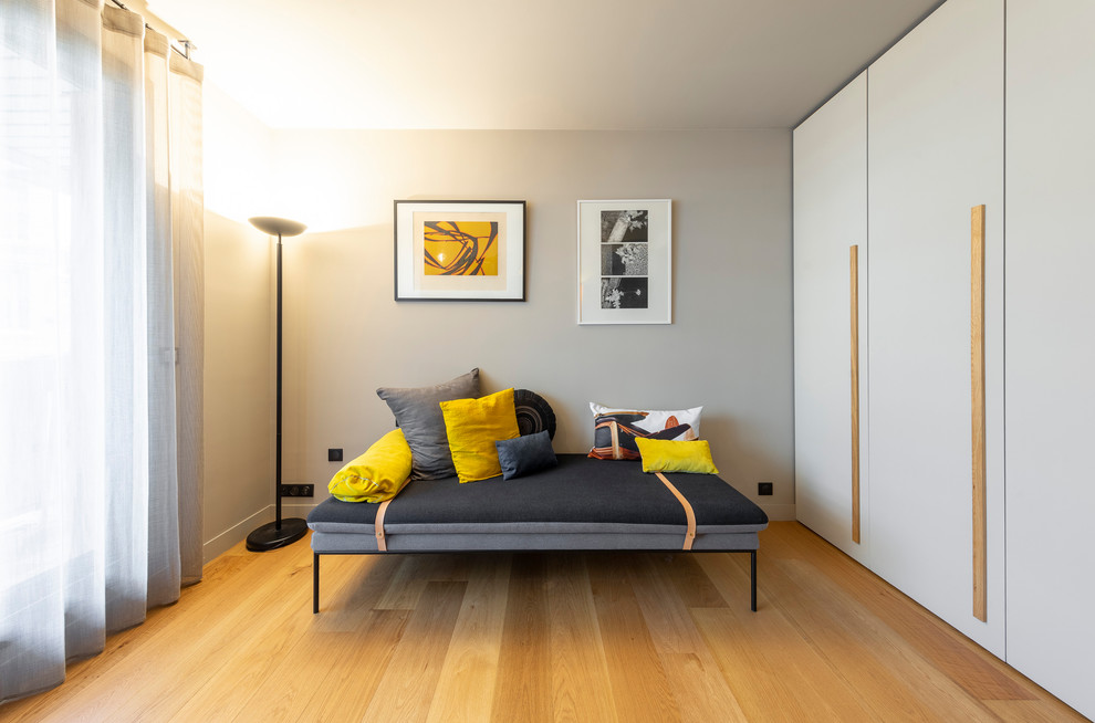 Foto de habitación de invitados moderna de tamaño medio sin chimenea con paredes beige, suelo de madera clara y suelo marrón