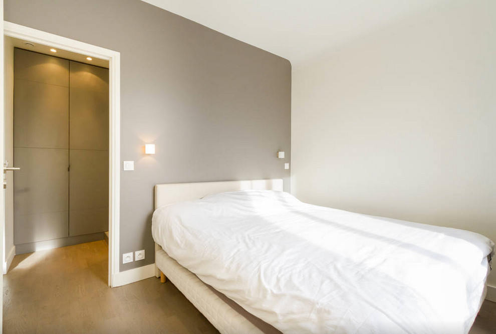 Inspiration pour une chambre parentale design de taille moyenne avec un mur gris, parquet clair et un sol marron.