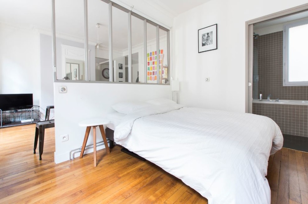 Ejemplo de dormitorio principal actual de tamaño medio con paredes blancas, suelo de madera en tonos medios, chimenea de esquina y suelo marrón
