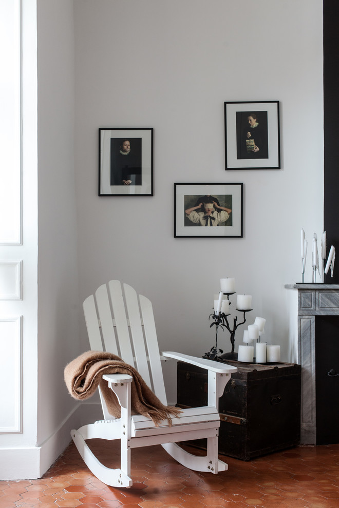 Cette photo montre une petite chambre d'amis tendance avec un mur blanc, tomettes au sol, une cheminée standard et un manteau de cheminée en pierre.