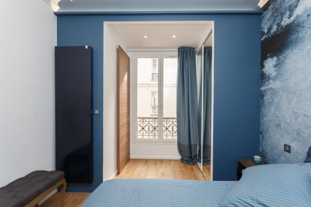 Ejemplo de dormitorio principal actual pequeño con paredes azules, suelo de madera clara y papel pintado