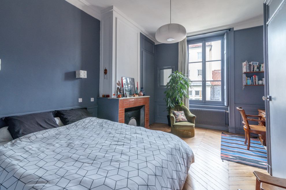 Foto de dormitorio principal actual de tamaño medio con paredes azules, suelo de madera en tonos medios, todas las chimeneas, marco de chimenea de ladrillo y boiserie