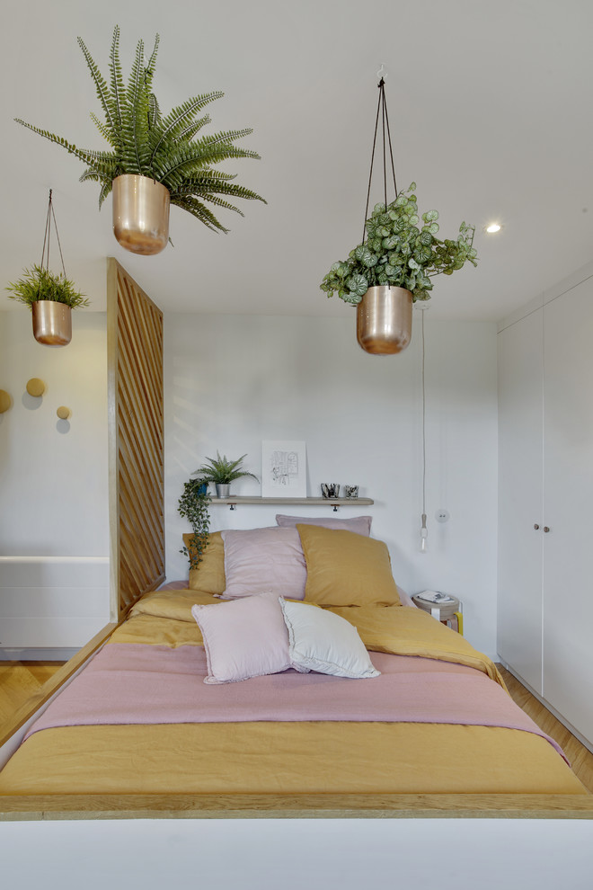 Modelo de dormitorio principal bohemio pequeño sin chimenea con paredes blancas, suelo de madera clara y suelo marrón
