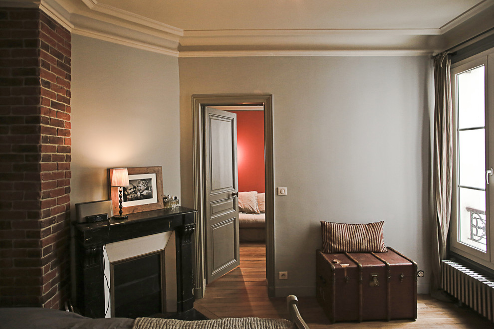 Foto de dormitorio principal retro de tamaño medio con paredes grises, suelo de madera en tonos medios, chimenea de esquina y marco de chimenea de piedra