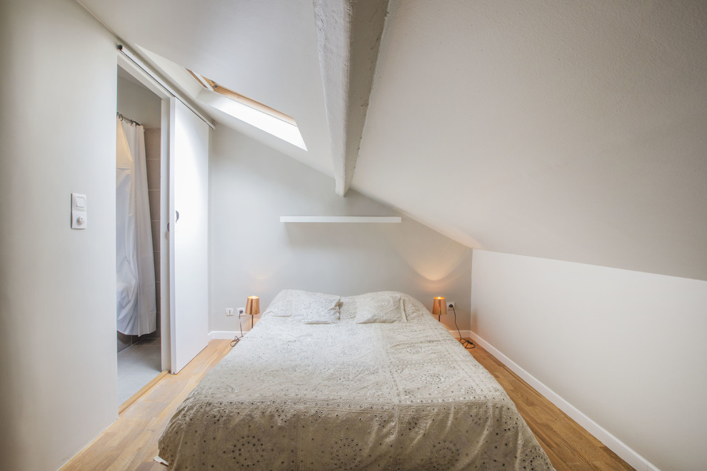 Imagen de dormitorio contemporáneo de tamaño medio con paredes blancas, suelo de madera en tonos medios y techo inclinado