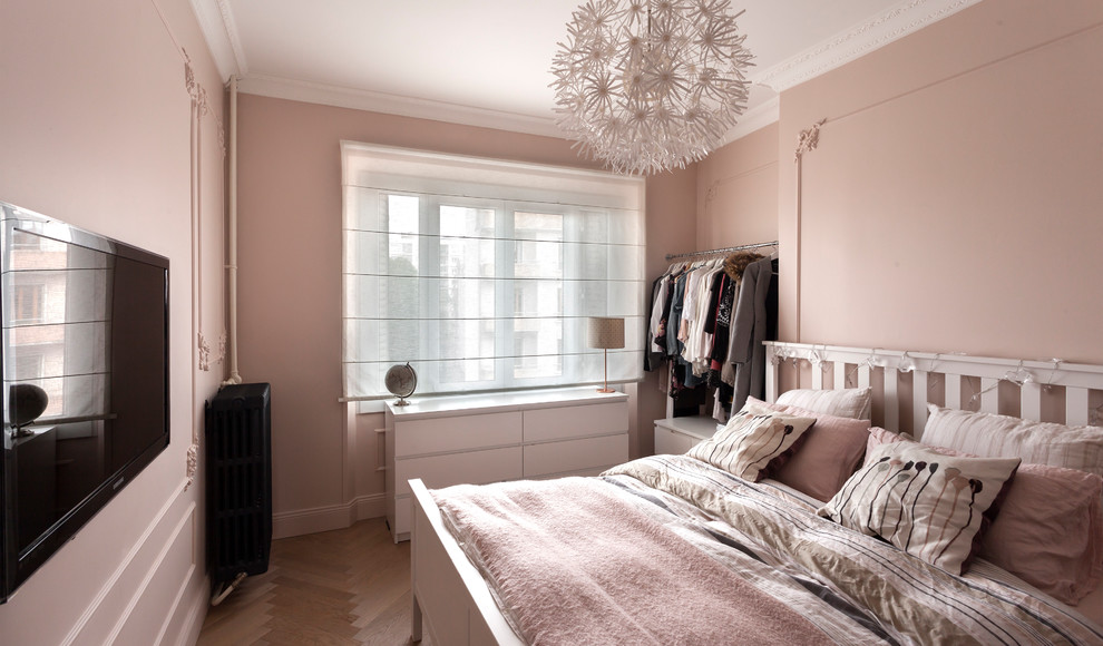 Bild på ett skandinaviskt sovrum, med rosa väggar, mellanmörkt trägolv och brunt golv