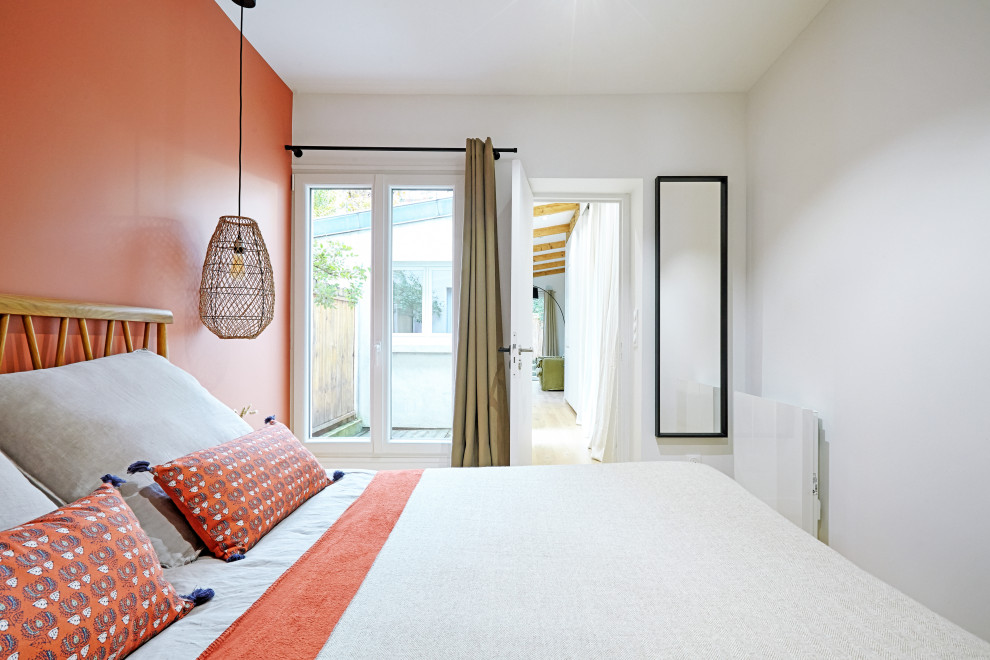 Modelo de dormitorio principal moderno de tamaño medio sin chimenea con parades naranjas, suelo de madera clara y suelo beige