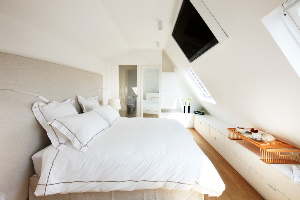 Diseño de dormitorio televisión actual de tamaño medio con paredes blancas y suelo de madera en tonos medios