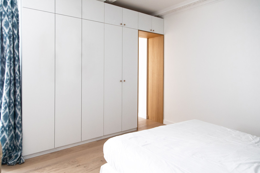 Mittelgroßes Hauptschlafzimmer ohne Kamin mit weißer Wandfarbe, braunem Holzboden und beigem Boden in Sonstige