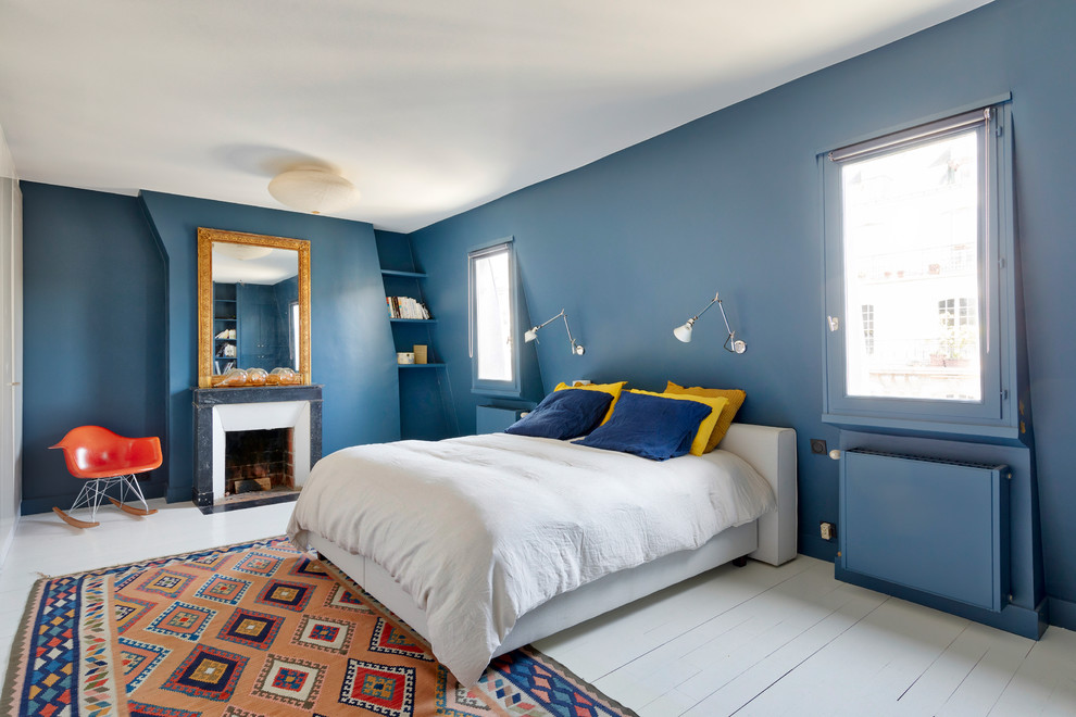 Stilmix Hauptschlafzimmer mit blauer Wandfarbe, gebeiztem Holzboden, Kamin, Kaminumrandung aus Backstein und weißem Boden in Paris