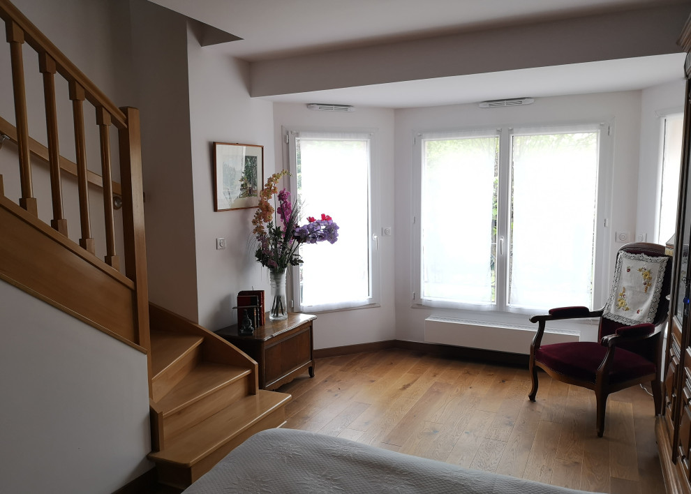 Landhaus Schlafzimmer mit weißer Wandfarbe, hellem Holzboden und braunem Boden in Paris