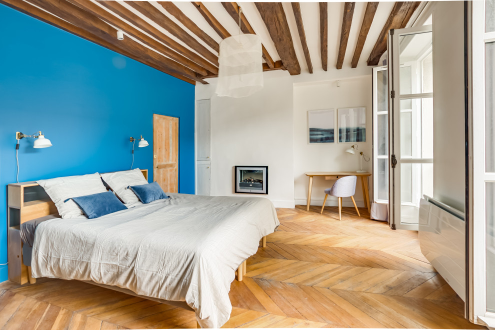 Modelo de dormitorio nórdico con paredes azules, suelo de madera en tonos medios, chimenea de doble cara y suelo marrón