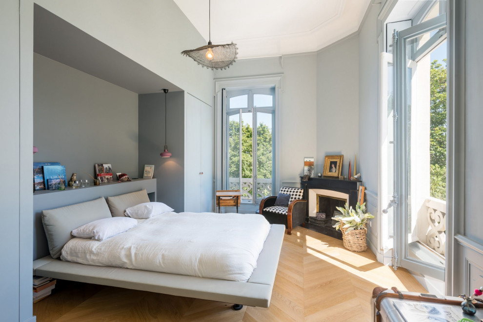 Großes Modernes Hauptschlafzimmer mit grauer Wandfarbe, hellem Holzboden, Eckkamin, Kaminumrandung aus Beton und beigem Boden in Lyon