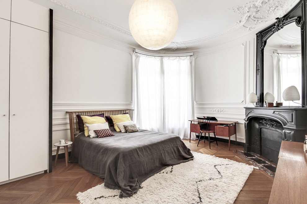 Klassisches Schlafzimmer mit weißer Wandfarbe, braunem Holzboden und Eckkamin in Paris