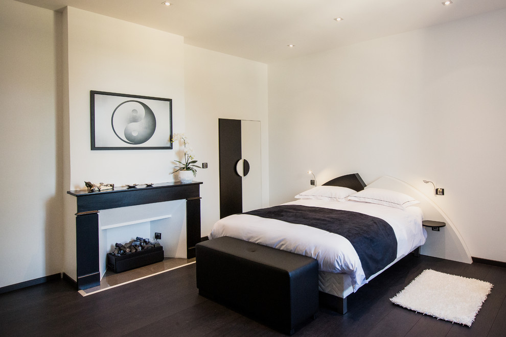 Стильный дизайн: хозяйская спальня среднего размера в современном стиле с белыми стенами, стандартным камином, темным паркетным полом и фасадом камина из дерева - последний тренд
