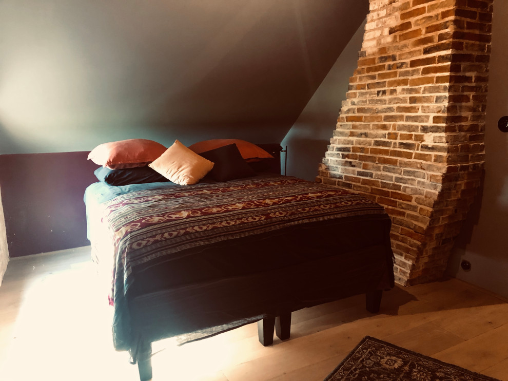 На фото: гостевая спальня среднего размера, (комната для гостей) в стиле кантри с серыми стенами, светлым паркетным полом, печью-буржуйкой и фасадом камина из кирпича