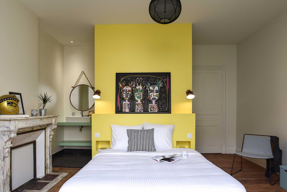 Modelo de dormitorio principal actual con paredes amarillas, suelo de madera en tonos medios, todas las chimeneas y suelo marrón