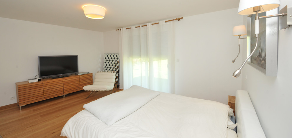 Aménagement d'une chambre parentale contemporaine avec un mur blanc et un sol en bois brun.