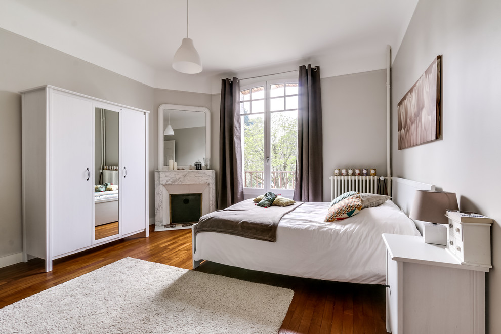 Diseño de habitación de invitados clásica grande con paredes blancas, suelo de madera en tonos medios, suelo marrón, chimenea de esquina y marco de chimenea de piedra