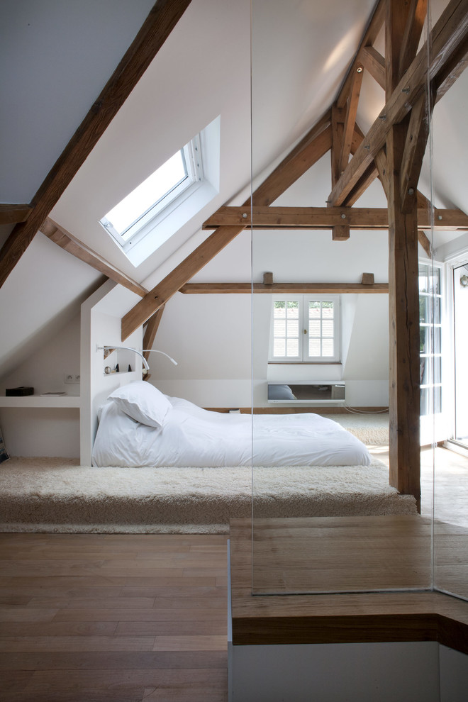 Modelo de dormitorio tipo loft y blanco y madera rústico de tamaño medio con paredes blancas, suelo de madera en tonos medios, techo inclinado y suelo marrón