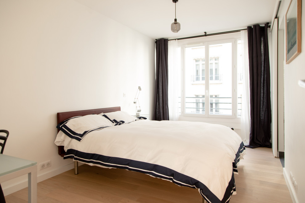 Modelo de dormitorio principal moderno de tamaño medio sin chimenea con paredes blancas, suelo de madera clara y suelo beige