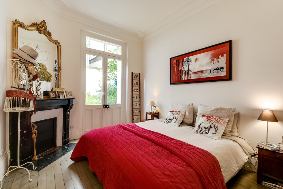 Eklektisches Hauptschlafzimmer mit weißer Wandfarbe, Eckkamin, gebeiztem Holzboden und Kaminumrandung aus Stein in Paris
