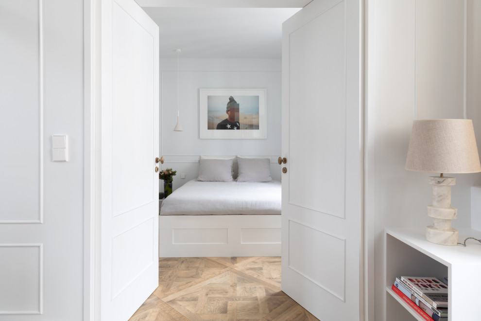 Пример оригинального дизайна: спальня в современном стиле с белыми стенами, паркетным полом среднего тона, коричневым полом и панелями на части стены