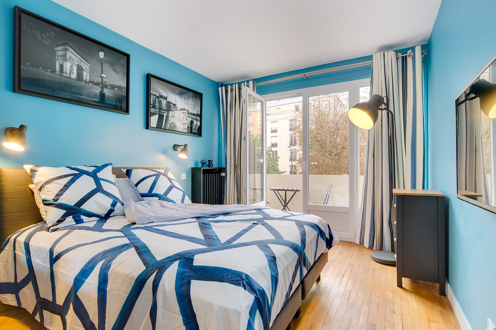 Imagen de dormitorio principal actual de tamaño medio sin chimenea con paredes azules y suelo de madera clara