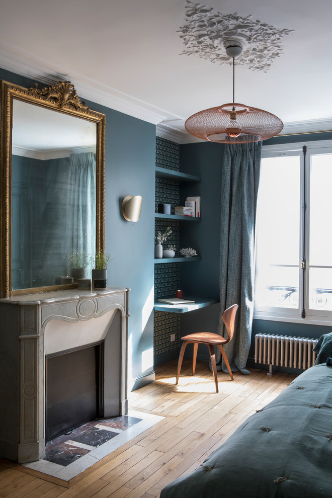 Idée de décoration pour une petite chambre parentale design avec un mur bleu, parquet clair, une cheminée d'angle, un manteau de cheminée en pierre et un sol beige.