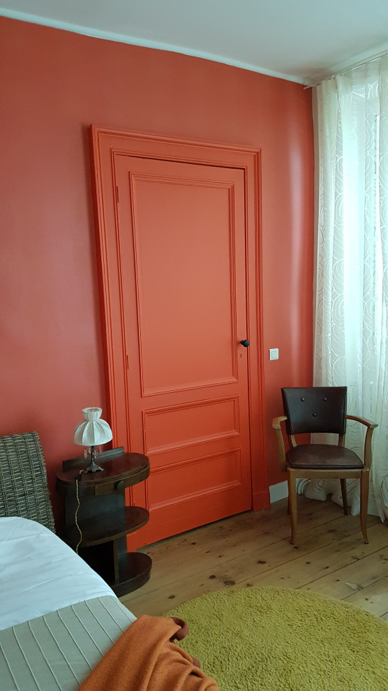 Cette photo montre une grande chambre parentale rétro avec un mur orange, un sol en bois brun et du papier peint.