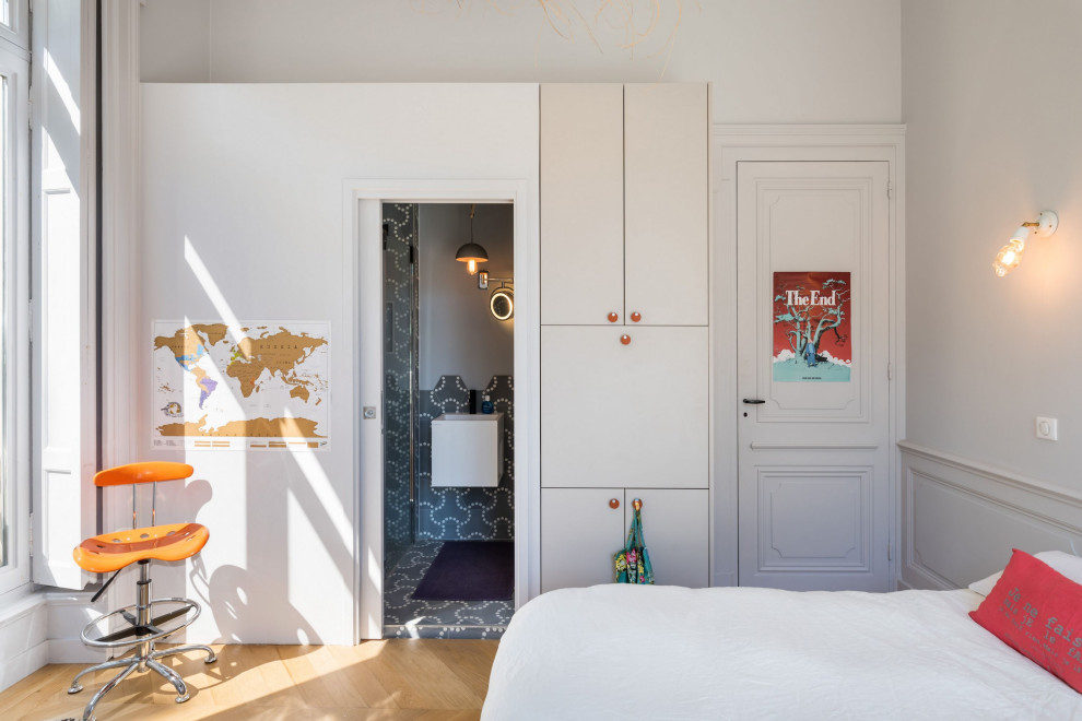 Modelo de dormitorio actual pequeño con paredes blancas, suelo de madera clara, chimenea de esquina, marco de chimenea de hormigón y suelo beige