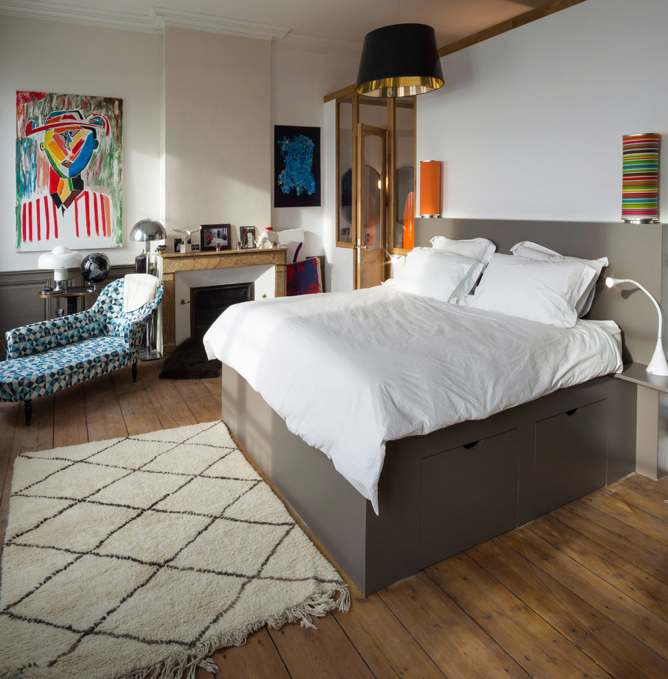 Bild på ett funkis sovrum, med vita väggar, mörkt trägolv, en standard öppen spis, en spiselkrans i sten och brunt golv