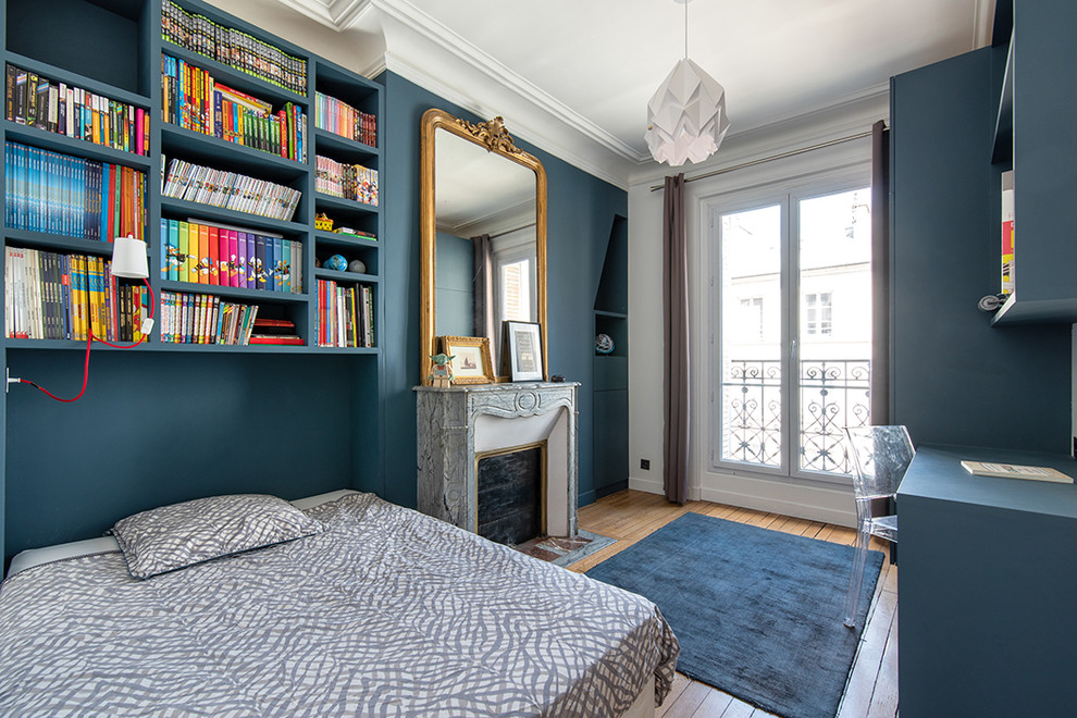 Exemple d'une chambre chic avec un mur bleu, un sol en bois brun, une cheminée standard, un manteau de cheminée en pierre et un sol marron.