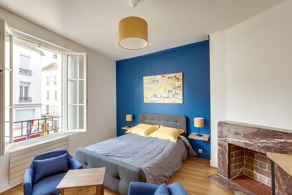 Cette photo montre une chambre tendance avec une cheminée standard, un sol marron et un mur bleu.