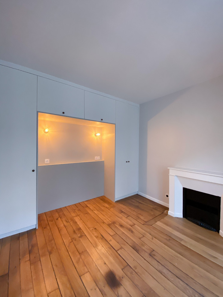 Réalisation d'une chambre parentale design de taille moyenne avec un mur gris, parquet foncé, une cheminée standard, un manteau de cheminée en plâtre et un sol marron.