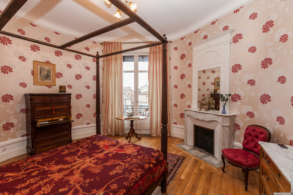 Imagen de dormitorio principal tradicional de tamaño medio con paredes rojas, suelo de madera clara, todas las chimeneas y marco de chimenea de piedra