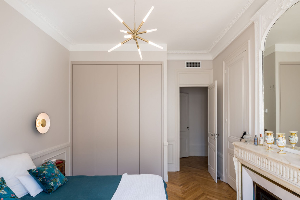 Mittelgroßes Klassisches Hauptschlafzimmer mit beiger Wandfarbe, braunem Holzboden, Kamin, Kaminumrandung aus Stein und vertäfelten Wänden in Lyon