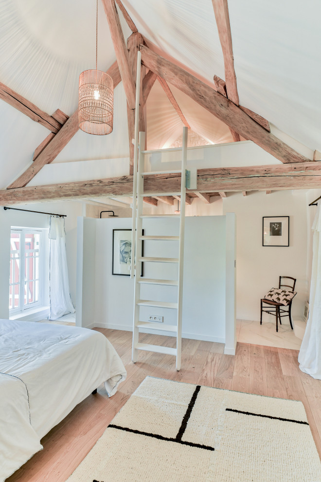 Aménagement d'une chambre campagne avec un mur blanc, un sol en bois brun, un sol marron, poutres apparentes et un plafond voûté.