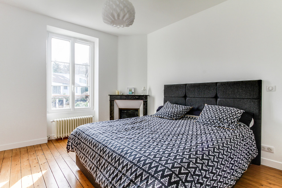 Diseño de dormitorio principal escandinavo con paredes blancas, suelo de madera en tonos medios, chimenea de esquina, marco de chimenea de piedra y suelo beige