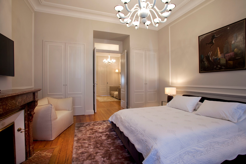 Ejemplo de dormitorio principal actual grande con paredes beige, suelo de madera en tonos medios, todas las chimeneas y marco de chimenea de piedra