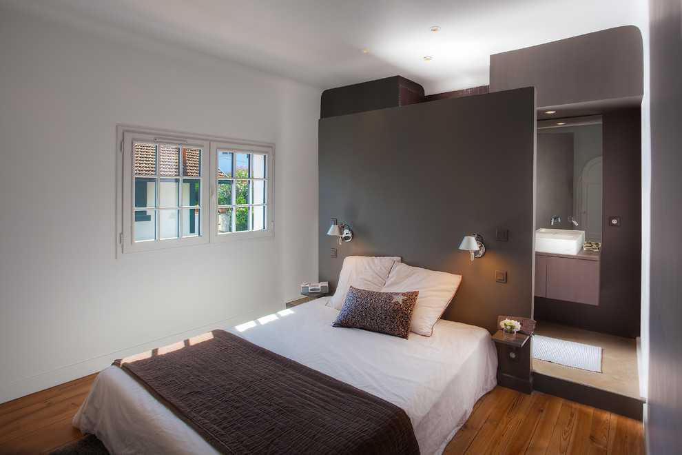 Modelo de dormitorio actual sin chimenea con paredes blancas y suelo de madera en tonos medios